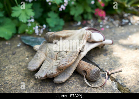 In pelle guanti da giardinaggio e un di legno trattati giardinaggio frattazzo su una parete del giardino in estate, UK. Foto Stock