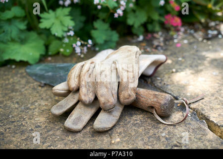 In pelle guanti da giardinaggio e un di legno trattati giardinaggio frattazzo su una parete del giardino in estate, UK. Foto Stock