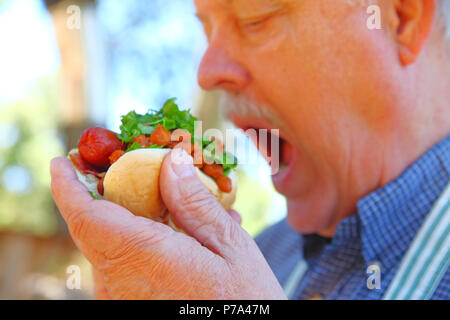 Uomo di mangiare un hot dog e rabboccato con peperoncino fagioli e tritato lattuga Foto Stock
