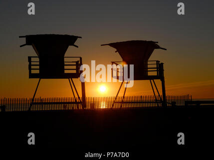 Lifeguard towers stagliano con regolazione del sole Huntington Beach California Foto Stock