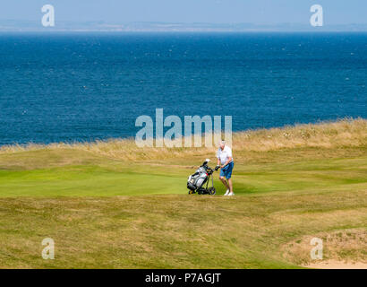 A North Berwick, East Lothian, Scozia, Regno Unito, 5 luglio 2018. I golfisti spingendo un carrello da golf sul Glen Golf accanto a Firth of Forth Foto Stock