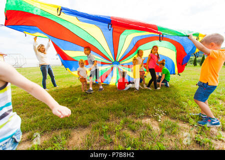 Contenti i bambini sventolano rainbow parachute Foto Stock
