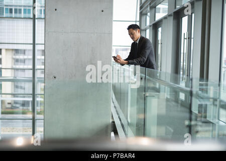 Imprenditore tramite telefono mobile appoggiata sulla ringhiera Foto Stock