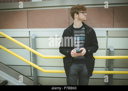 Giovane uomo appoggiato sulla ringhiera tramite telefono cellulare Foto Stock