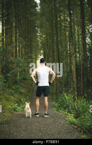 Uomo in piedi con il suo cane nella lussureggiante foresta Foto Stock