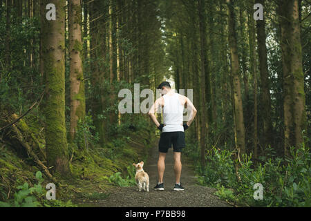 Uomo in piedi con il suo cane nella lussureggiante foresta Foto Stock