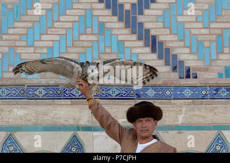 Il kazako uomo in abiti tradizionali visualizzando il suo gufo reale (Bubo bubo), Turkestan, regione sud, Kazakistan Foto Stock