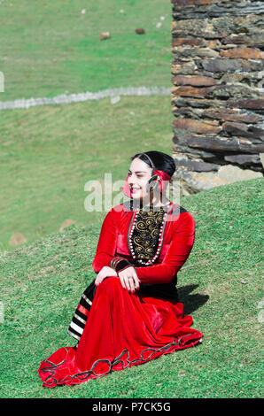 Georgian donna da un gruppo folcloristico di seduta sul terreno di fronte a una torre, per il solo uso editoriale, Ushguli, regione di Svaneti, Georgia Foto Stock