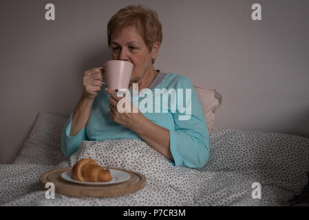 Senior donna con caffè e colazione in camera da letto Foto Stock