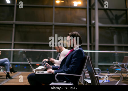 Imprenditore utilizzando il telefono cellulare mentre si lavora sul computer portatile in area di attesa Foto Stock