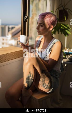 Donna con il caffè mentre si utilizza il telefono cellulare a casa Foto Stock