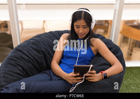 Donna con tavoletta digitale mentre si ascolta la musica sulle cuffie Foto Stock
