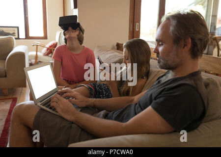 Padre e figlie utilizzando dispositivi elettronici in salotto Foto Stock