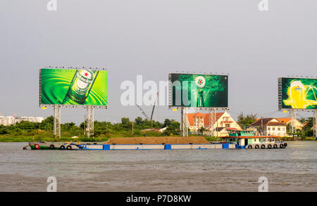 Trasporto alla rinfusa inclus. Il trasporto di un carico sul fiume Saigon con la mitica Heineken cartelloni in background., Ho Chi Minh City, Vietnam. Foto Stock