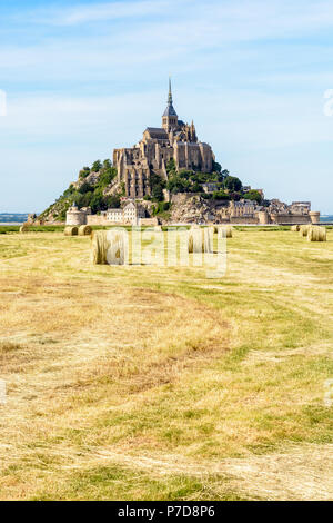 Il Mont Saint Michel isola di marea in Normandia, Francia, con le balle di paglia in un campo in primo piano sotto un cielo blu con nuvole fibroso. Foto Stock