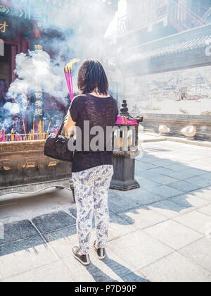 Giovane donna tenere grandi bruciare bastoncini di incenso mentre pregando presso il Tempio Taoista della Regina del Cielo, Tianjin, Cina Foto Stock