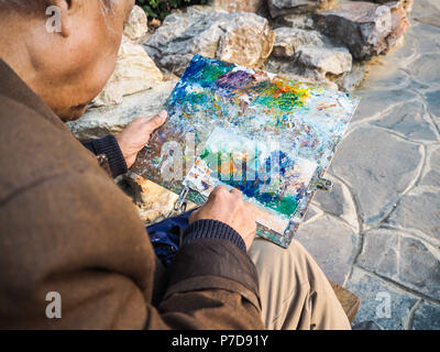 Ritirato uomo asiatico usando un coltello di verniciatura per fare un dipinto ad olio, Nanjing, Cina di un tempio cinese Foto Stock