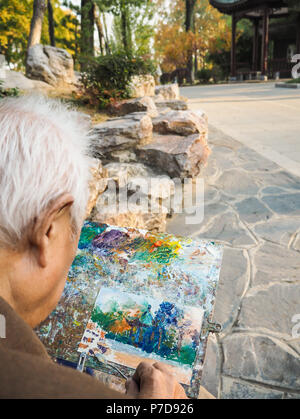 Ritirato uomo asiatico usando un coltello di pittura per dipingere un tempio tradizionale Cinese in Xuanwu lake park, Nanjing, Cina Foto Stock