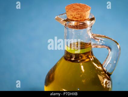 Cercando una bella piccola bottiglia di vetro con qualità premium olio vergine di oliva chiusa con un tappo di sughero. Vasetto di olio vicino isolata con sfondo blu. Foto Stock