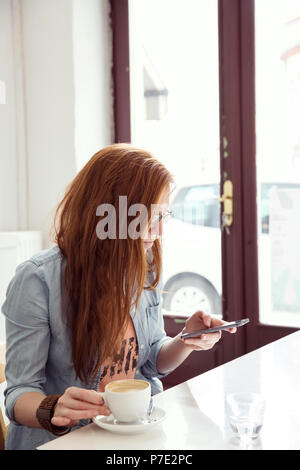 Giovane donna utilizzando il telefono cellulare in cafe Foto Stock