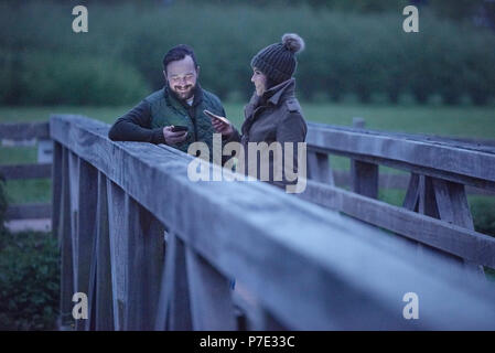 L uomo e la donna sul ponte rurale al tramonto guardando gli smartphone Foto Stock