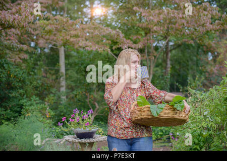 Donna in giardino a bere dal bicchiere Foto Stock