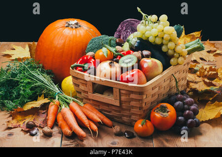 Assortimento di carni fresche e mature autunno di frutta e verdura su una tavola in legno rustico con sfondo nero Foto Stock