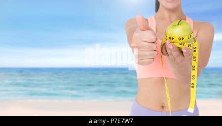 Donna di peso misurazione con nastro di misurazione sulla vita e l'azienda Apple su estate spiaggia Foto Stock