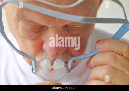 Senior man tenere premuto sleep apnea copricapo fino al suo volto Foto Stock