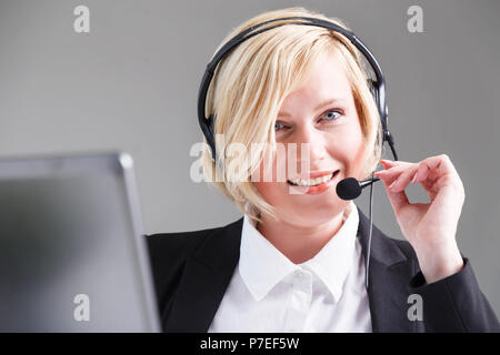 Donna sorridente, operatore di call center vestita di nero elegante completo con cuffie auricolari Foto Stock