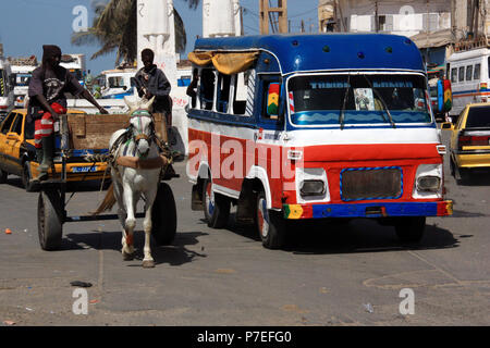 Movimentata strada principale di Saint-Louis du Sénégal: Minibus il sorpasso di due uomini alla guida di un carrello a cavallo Foto Stock