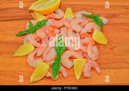 Cucinati e sgusciati gamberi con fette di limone e foglie di basilico sul tagliere. Fotografia di cibo. Cibo sano. Bio ricetta Foto Stock