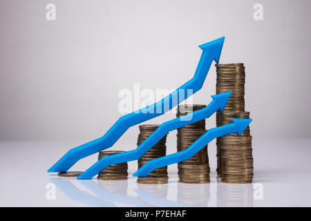 Impilate le monete d'oro con crescente le frecce blu su sfondo riflettente Foto Stock