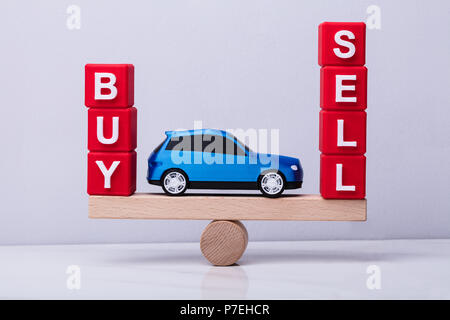 Auto blu tra e comprare e vendere i blocchi cubici in equilibrio su altalena in legno Foto Stock