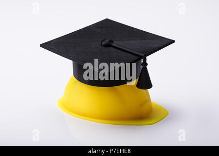 Close-up di graduazione Hat su Hardhat giallo su sfondo bianco Foto Stock