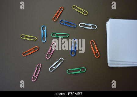 Carta colorata fascette indicate con un punto interrogativo e con fogli di carta bianca per la registrazione su un marrone sfondo opaco. Foto Stock