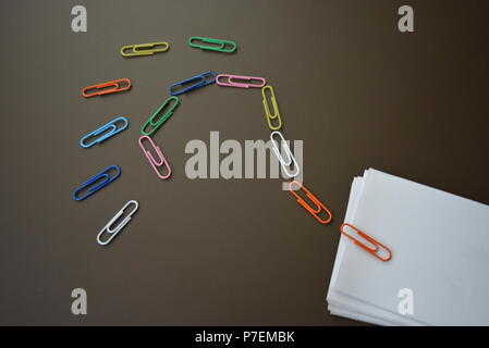 Carta colorata fascette indicate con un punto interrogativo e con fogli di carta bianca per la registrazione su un marrone sfondo opaco. Foto Stock