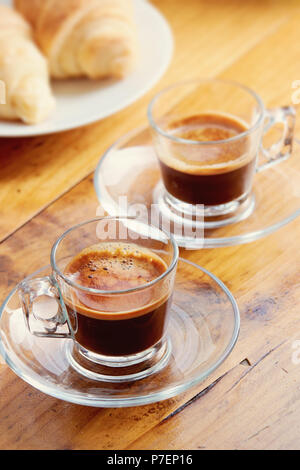 Due tazze di caffè espresso con un croissant sul vecchio tavolo in legno Foto Stock