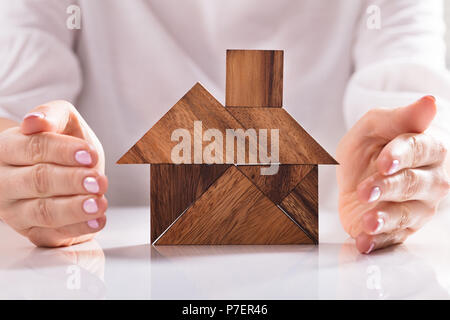 Close-up di una donna di mano la protezione di casa fatta di legno Puzzle Tangram su scrivania Foto Stock