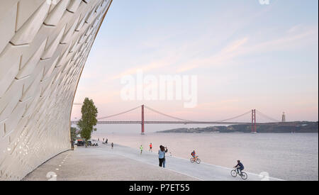 Passi sul lungomare e sinuosa facciata con pista ciclabile e la vista del ponte. MAAT, Lisbona, Portogallo. Architetto: UN LA, 2016. Foto Stock