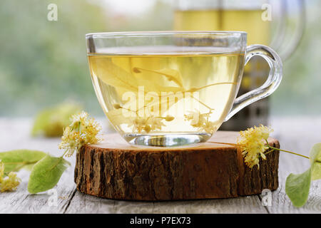 Tazza di tè freschi da Linden foglie in piatti trasparente su un supporto in legno, close-up Foto Stock