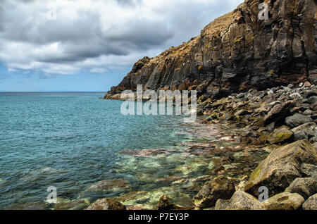 Rocky wild Madeira Beach con big pink, marrone, verde e grigio pietre. Oceano colorato letto può essere chiaramente visto attraverso pulite acque turchesi dell'Oceano Atlantico Foto Stock
