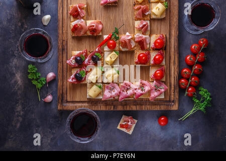 Antipasti tabella con antipasti italiani spuntini e il vino in bicchieri. Spaghetti o autentici tradizionali tapas spagnoli, varietà di formaggio scheda sopra di cemento grigio Sfondo. Vista superiore, laici piatta Foto Stock