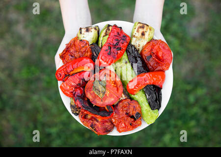 Mani femminili tenere la piastra grigliata di verdure di stagione, vista da sopra. Foto Stock