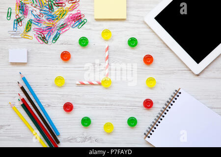 Il concetto di istruzione, torna a scuola. Nove ore di guardia. Orologio fabbricato di coloratissimi dolci caramelle, accessori per studio bianco su sfondo di legno, da Foto Stock