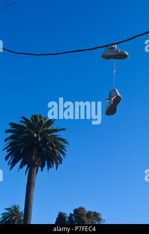 Devianza: Bianco sport fashion alta cima sneakers appesa a una California del sud linea di potenza con un albero di palma in background su un cielo blu chiaro giorno Foto Stock