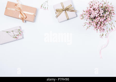 Festosa femminile rosa laici piatta con bouquet di fiori di gypsophila e confezioni regalo. Vista superiore telaio su sfondo bianco con copia spazio. Foto Stock