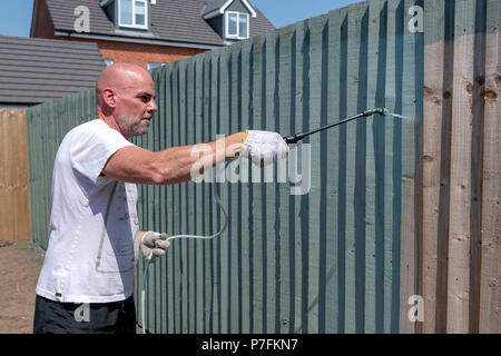 Uomo con uno spruzzatore di vernice per dipingere un giardino recinto verde Foto Stock
