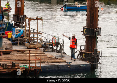 Schull, West Cork, Irlanda. 6 Luglio, 2018. Un lavoratore è mostrato di dirigere la costruzione barge in posizione per consentire ai contraenti di installare il nuovo pontile in Schull Harbour. Il lavoro è prevista per le 4 settimane e costano circa € 500.000. Credito: Andy Gibson/Alamy Live News. Foto Stock