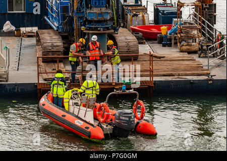 Schull, West Cork, Irlanda. 6 Luglio, 2018. Lavoratori edili e ingegneri di controllare la posizione della costruzione chiatta per facilitare l'installazione di pali che supporterà il nuovo pontile in Schull Harbour. Il lavoro è prevista per le 4 settimane e costano circa € 500.000. Credito: Andy Gibson/Alamy Live News. Foto Stock